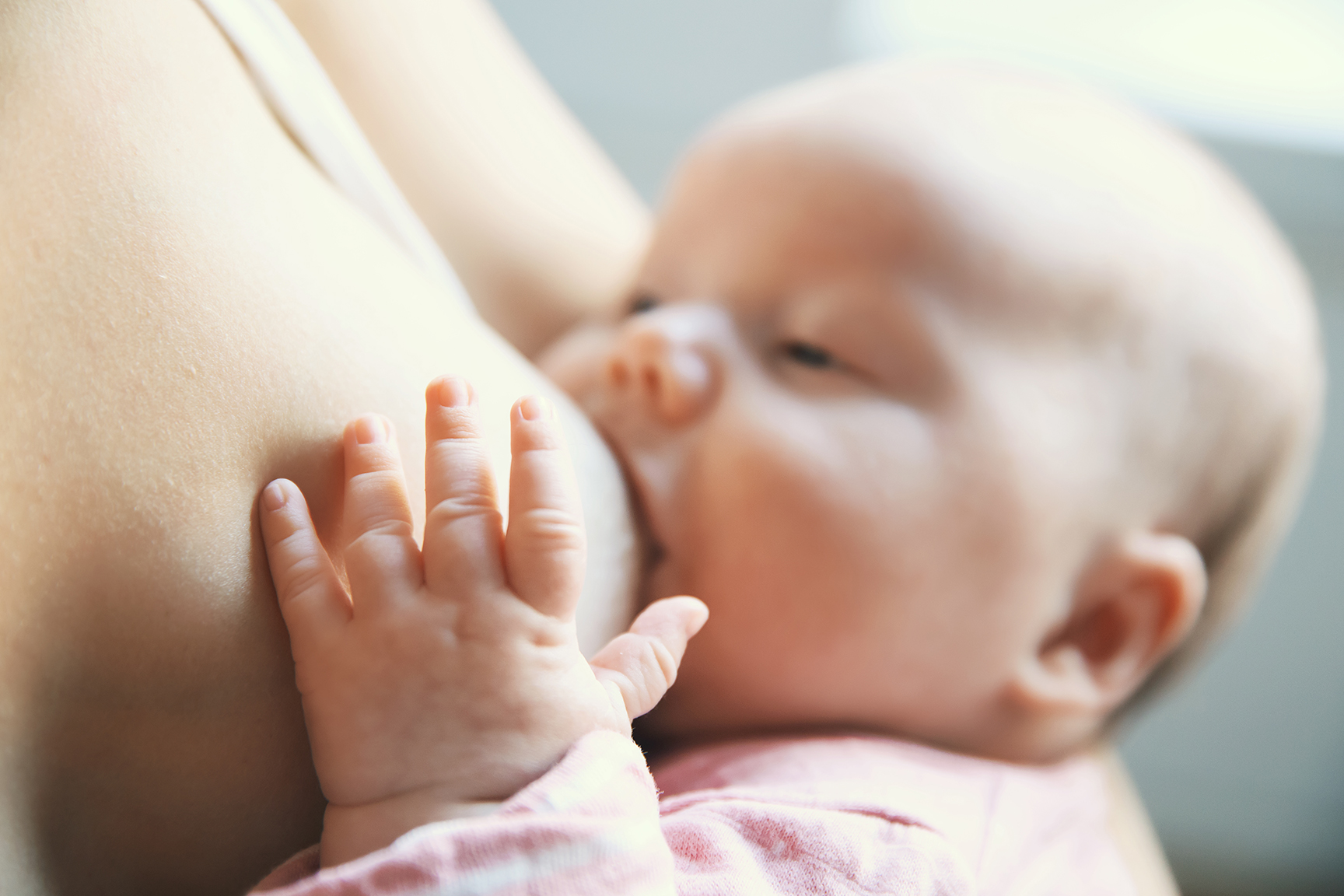 Baby eating mother's milk. Mother breastfeeding baby. Young woman nursing and feeding baby. Concept of lactation infant. Focus on the little child's pen, blurred background.